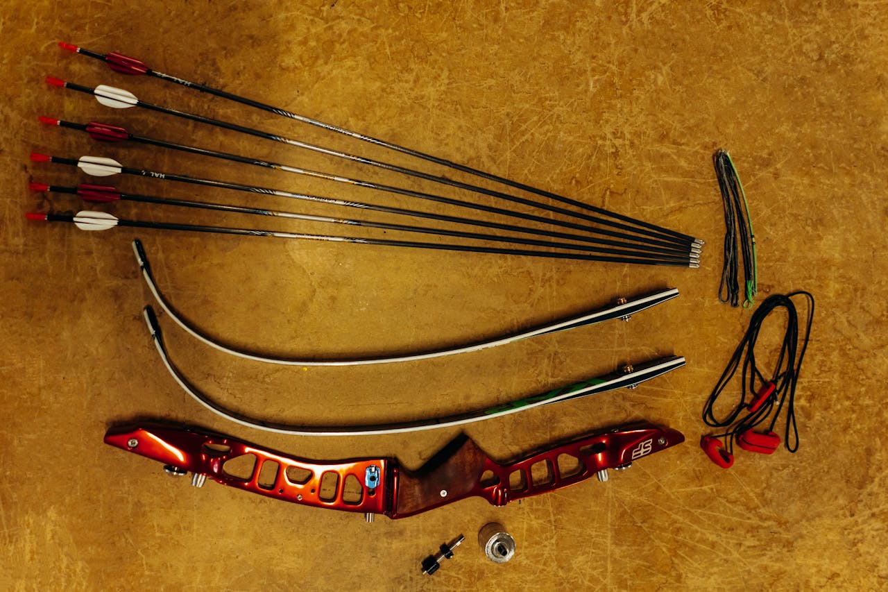 Top view of unassembled recurve bow and arrows laid out on a surface, highlighting archery equipment details.